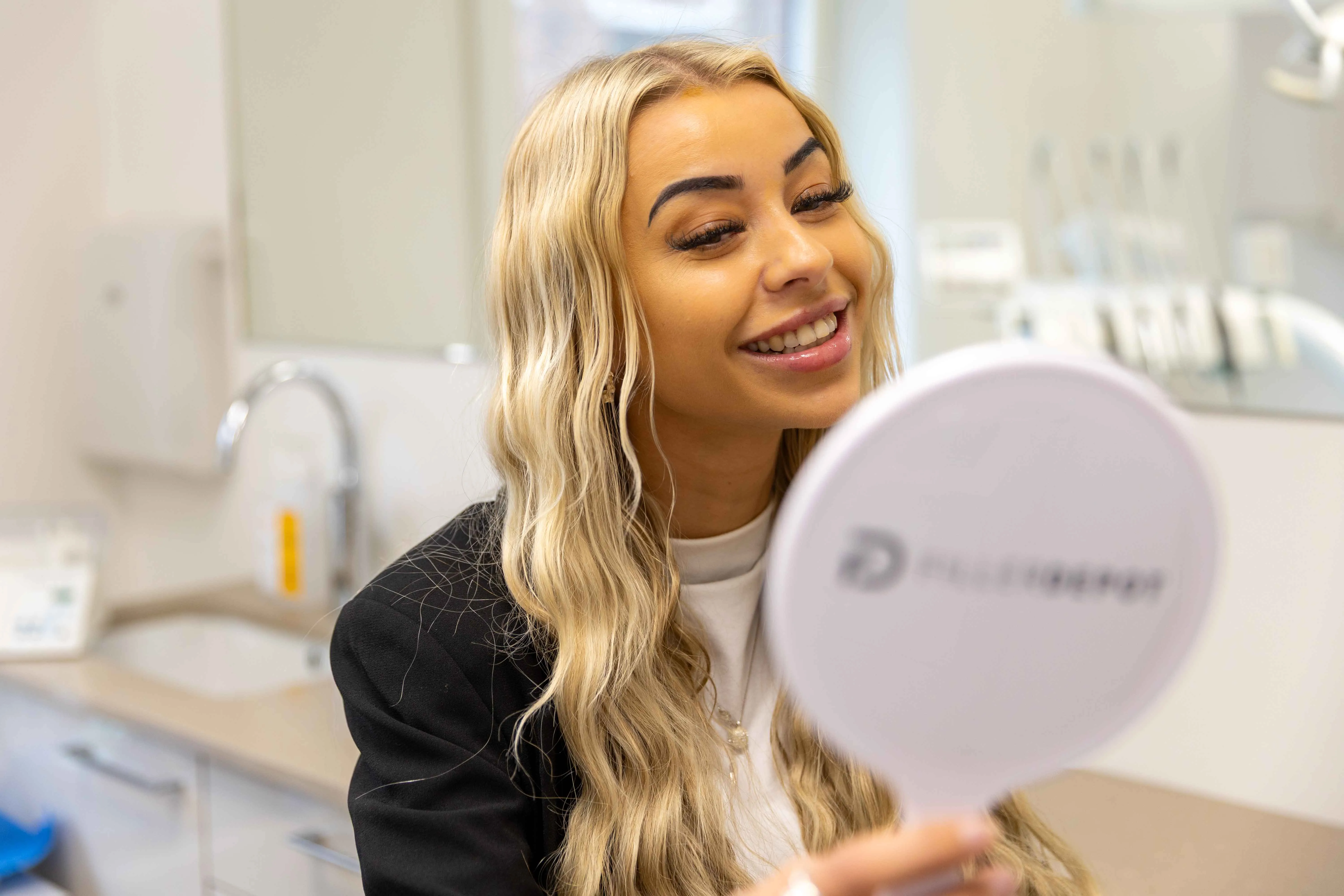 Glad patient kigger på sit smil i et håndspejl hos City Tandlægerne